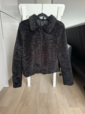 Svart teddyjacka med krage - Mysig svart teddyjacka med klassisk krage och knäppning framtill. Jackan har en mjuk och fluffig. Passar perfekt till kyligare dagar och ger en trendig look. Enkel och stilren design utan synliga detaljer.