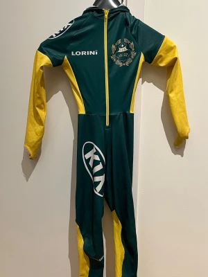 Grön och gul cykeldräkt Lorini 140 - Säljer en grön och gul cykeldräkt från Lorini i storlek 140. Dräkten har dragkedja framtill, långa ärmar och ben samt tryckta loggor och klubbmärke. Materialet är syntet och passar perfekt för träning eller tävling.