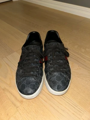 Gucci sneakers med monogram och röd detalj - Säljer ett par Gucci-skor med monogram  i storlek 43. Använda men i ett hyfsat skick. Klassisk stil och bra kvalitet. Kan sänkas vid snabb affär.