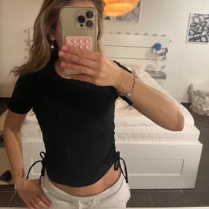 Svart ribbad topp med snörning Paul Mark - Svart ribbad topp från Paul Mark med korta ärmar och snörning i sidorna som ger en snygg croppad look, och man kan dra åt. Står att den är i m men den passar som s!