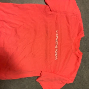 Korallrosa t-shirt från LOOP NICOTINE PCHS - Säljer en korallrosa t-shirt från LOOP NICOTINE PCHS med tryck på bröstet. T-shirten har rund halsringning och korta ärmar. Skön och enkel modell i mjuk bomull, perfekt till jeans eller shorts.