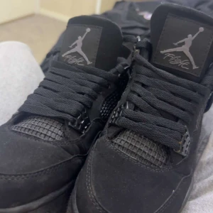 Svarta Nike Jordan 4 sneakers - Säljer ett par svarta Nike Jordan 4 sneakers med klassisk Jumpman-logga på plösen. Skorna har snörning, meshdetaljer och robust design. Materialet är en mix av mocka och syntet, perfekt för dig som gillar streetwear och sportig stil.