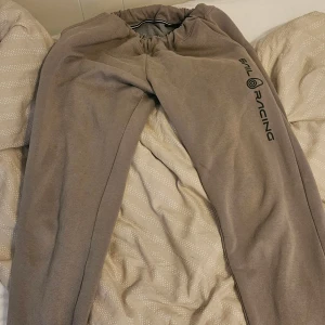 Grå mjukisbyxor från Sail Racing M - Beiga mjukisbyxor från Sail Racing i storlek M. Byxorna har resår i midjan, en bakficka och Sail Racing-logga längs ena benet. Tillverkade i mjukt material som känns skönt mot huden. Perfekta för chill dagar eller när du vill vara bekväm.
