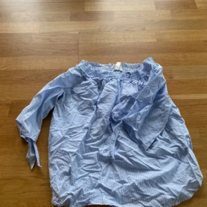 Blåvit offshoulder blus med knytärm - Säljer en söt blåvit randig offshoulder blus med  resår upptill och knytning vid ärmsluten. Blusen har trekvartsärmar. 
