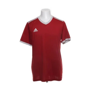 Röd Adidas fotbollströja herr - Klassisk röd fotbollströja från Adidas med vita detaljer på axlar och ärmslut. Tröjan har v-ringning och är tillverkad i 100% återvunnen polyester, vilket gör den lätt och andas bra under match eller träning. Adidas-logga på bröstet.