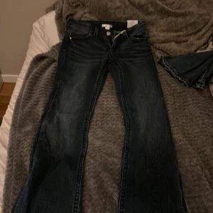 Blå bootcut jeans från Gina Tricot - Snygga mörkblå bootcut jeans från Gina Tricot i modellen 'low boot embroidery jeans'. Låg midja, klassisk femficksdesign och coola silvriga detaljer vid fickorna. Jeansen är gjorda i bomull och har dragkedja och knapp framtill.