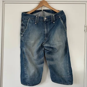 Levi's loose fit jeansshorts - Säljer ett par blå jeansshorts från Levi's med loose fit och klassisk femficksdesign. Shortsen har slitna detaljer, stora bakfickor och knäppning med metallknapp. Perfekta för en chill och avslappnad stil.
