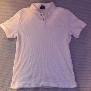 Vit kortärmad piké från H&M - Vit pikétröja från H&M i slim fit-modell. Skjortan har korta ärmar, klassisk krage och två knappar framtill. Materialet är strukturerat och känns mjukt mot huden. Perfekt för en clean och fräsch look.