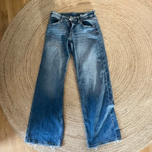 Wide leg low jeans från H&M - Säljer ett par blå wide leg jeans från H&M i storlek 164. Jeansen har låg midja och justerbar midja för perfekt passform. Klassisk femficksmodell i denim med snygg tvätt och raka, vida ben. Perfekta för en avslappnad och trendig look.