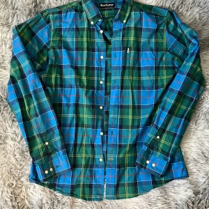 Rutig skjorta från Barbour blå/grön - Snygg rutig skjorta från Barbour i blått och grönt med inslag av gult och rött. Skjortan har lång ärm, klassisk krage, knappar framtill och bröstficka med Barbour-logga. Skräddarsydd passform och tillverkad i mjuk bomull.