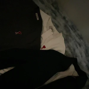 Ami Paris t-shirt med rött hjärta - Säljer en stilren t-shirt från Ami Paris med det ikoniska röda hjärtat broderat på bröstet. Finns i både svart och vit. Klassisk passform och rund halsringning, perfekt för en clean och trendig look.