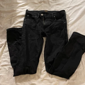 Svarta jeansbyxor från Lee - Svarta jeansbyxor från Lee med klassisk femficksdesign och raka ben. Byxorna har knapp och dragkedja framtill samt bälteshällor. Perfekta för en stilren och enkel look.Storlek: 29/32