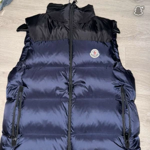 Moncler dunväst marinblå - Snygg dunväst från Moncler i svart och marinblått med hög krage och dragkedja framtill. Västen har två praktiska fickor med dragkedja och klassisk Moncler-logga på bröstet. Perfekt för lager-på-lager och streetstyle. Moncler väst använd kanske 6 gånger size S moncler size 1 cond.9/10 nästan 10/10.