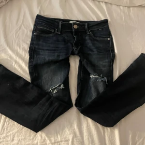 Mörkblå bootcut jeans med slitningar lågmidjade  - Superfina mörkblå jeans från kvalitetsmärket Mavi Jeans. De sitter riktigt snyggt på kroppen och har en lätt sliten look vid knäna som ger en trendig, avslappnad stil. Passar perfekt till både vardag och fest! Märket Mavi är känt för att ha fina och hållbara jeans. Jag har en galen rabatt!