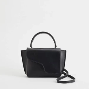 Svart axelväska i skinn - Stilren svart axelväska i skinn med ett unikt lock och både handtag och axelrem. Väskan har en minimalistisk design och passar perfekt för dig som gillar en clean look med snygga detaljer, väskan köptes för 3900. Meddela mig för fler bilder på väskan💞