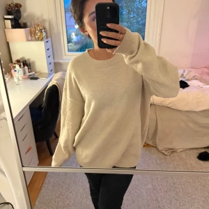 Beige oversized stickad tröja - Mysig och oversized stickad tröja i beige med rund halsringning och långa ärmar. Perfekt för lager-på-lager och chill dagar. Tröjan har en enkel och clean look med ribbade muddar vid ärmslut och nederkant. Är från Gina Young! 