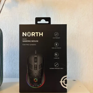 North M200 Gaming Mouse - North M200 Gaming Mouse är lättviktig (72g) och designad för gamers. Den har RGB LED-effekter, 12 800 DPI, 7 knappar, slitstark flätad kabel och 1000 Hz polling rate. Ergonomisk form för komfort under långa spelsessioner. Produkten är i nyskick i originalförpackning.