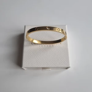 Guldigt armband  - Snyggt guldigt armband med stilrena detaljer. Armbandet är stelt och har infällda små stenar samt ingraverade symboler runt om. Perfekt accessoar för att lyfta din outfit med en lyxig touch. Lådan ingår ej.
