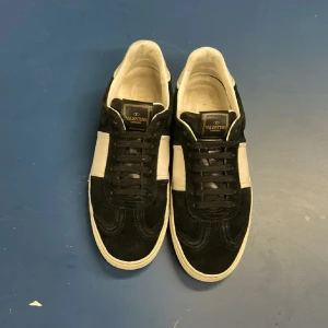 Valentino Garavani svartvita sneakers - Snygga sneakers från Valentino Garavani i svart mocka och vitt skinn. Klassisk låg modell med svarta snören och vit sula. Märkeslogga på plösen och stilren design som sticker ut. Perfekta för dig som gillar exklusiva och trendiga skor. Passar även 42 priset går att diskutera!