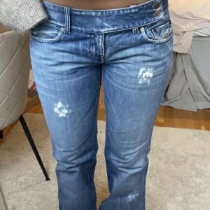 Lågmidjade blå bootcut jeans disel jeans  - Snygga lågmidjade blå jeans med bootcut passform och slitna detaljer på benen. Jeansen har klassisk femficksdesign och knäppning med två synliga knappar. Perfekta för en avslappnad och trendig look.