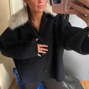 Mörkblå jacka med päls-krage - Mörkblå jacka från Zara med oversized passform och stora knappar framtill. Jackan har en fluffig, ljus fuskpäls-krage. Klassisk rak modell med långa ärmar. Aldrig använd, helt ny