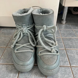 Ljusblåa Inuikii boots - Säljer ett par ljusblåa Inuikii moon boots med fluffigt foder och grova snören. Skorna är tillverkade i skinn och mocka, har platt sula och rund tå. Perfekta för kalla dagar med sin mysiga insida och coola look.
