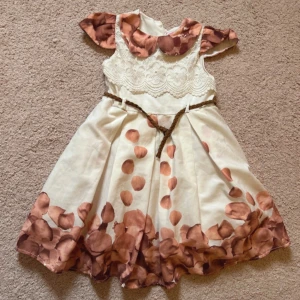 Vit och brun klänning från Enfetto - Supersöt vit klänning från Enfetto med bruna blommiga detaljer på krage och ärmar, samt stora bruna prickar och blommönster nertill. Överdelen har broderad spets och ett flätat bälte i midjan. Perfekt för vår och sommar! Aldrig använd 