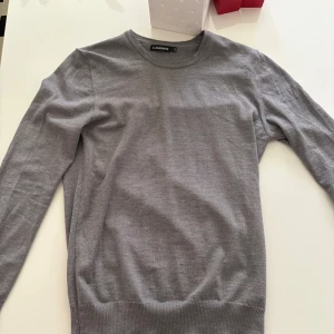 Grå stickad tröja från J.Lindeberg - ⚠️Använt endast två-tre gånger⚠️  ⚠️ Står att det är storlek L men passar perfekt som M ⚠️ Annars snygg grå stickad tröja från J.Lindeberg med diskret logga på bröstet. Tröjan har rund halsringning, ribbade muddar och lång ärm. Perfekt för lager-på-lager och passar till allt. Enkel och stilren design som funkar året runt.