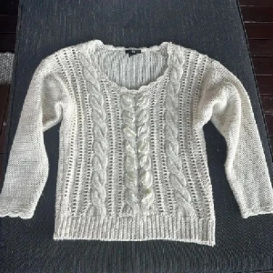 Vit stickad tröja med pärldetaljer H&M - Superfin vit stickad tröja från H&M med flätstickat mönster och pärlliknande detaljer framtill. Tröjan har rund halsringning och trekvartsärm. Perfekt för lager-på-lager och ger en mysig men ändå stylish vibe.