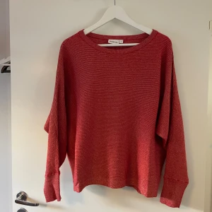 Röd och glittrig stickad tröja från Kappahl - Säljer en röd, glittrig stickad tröja från Kappahl i storlek L. Tröjan har en vid passform, rund halsringning och långa ärmar. Den är ribbstickad med diskreta ränder och passar perfekt för kyligare dagar.