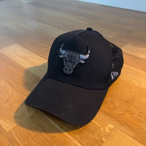 Svart Chicago Bulls keps från New Era - Svart keps från New Era med Chicago Bulls-logga framtill i svart och grått. Kepsen har böjd skärm och mesh-paneler bak för extra ventilation. Justerbar passform med snapback. Perfekt för dig som vill ha en sportig och stilren look.