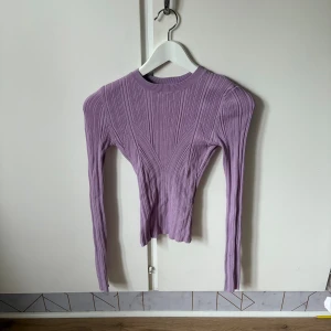 Lila ribbad topp med öppen rygg NA-KD - Säljer en lila långärmad topp från NA-KD i storlek XS. Toppen är ribbad och har en snygg croppad passform med en stor, rund öppning i ryggen. Materialet är mjukt och stretchigt, perfekt för dig som gillar trendiga detaljer och coola snitt.