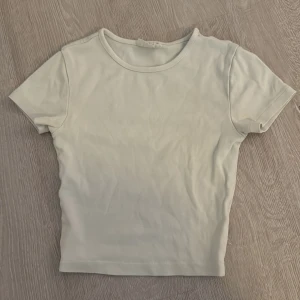 Vit T-shirt från Gina Tricot - Säljer en stilren vit T-shirt från Gina Tricot, kollektionen Basically Basic. Toppen har rund halsringning och korta ärmar, tillverkad i mjuk bomull som är skön mot huden. Perfekt att matcha med jeans eller kjol för en clean look.