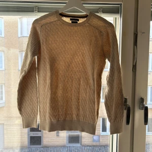 Beige stickad tröja Massimo Dutti - Säljer en beige stickad tröja från Massimo Dutti i extrafin bomull. Tröjan har ett diskret mönster, rund halsringning och ribbade muddar vid ärmslut och nederkant. Perfekt för lager-på-lager och snygg till jeans eller kjol.
