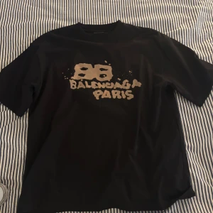 Svart Balenciaga Paris t-shirt M - Svart t-shirt från Balenciaga i bomull med beige tryck både fram och bak. Oversized fit med coolt grafiskt motiv och texten 'Balenciaga Paris' på bröstet. Perfekt statement-plagg för dig som gillar streetwear och designer. T-shirten är givetvis äkta och köpt på miinto.se kvitto finns, storlek M lite oversized (se bild) är 188cm 86kg