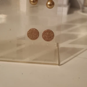 Glittriga runda örhängen i guld - Säljer ett par snygga örhängen i rund form med glittrig yta i guldton. Perfekta för dig som vill ha något enkelt men ändå iögonfallande. Stiftmodell som sitter bekvämt på örat och ger en cool touch till din stil.