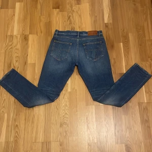 Blåa Tiger of Sweden slim fit jeans - Snygga blå jeans från Tiger of Sweden med klassisk femficksdesign och dragkedjegylf. Jeansen har en rak passform och är tillverkade i bomull med en touch av stretch för extra komfort. Perfekta för dig som gillar stilrena och tidlösa jeans.