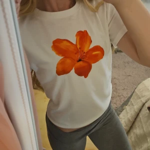 Vit baby-tee med orange blomma - Vit t-shirt med en stor, färgstark orange blomma tryckt på bröstet. Klassisk rund hals och korta ärmar. T-shirten har en clean look med fokus på det blommiga motivet framtill. Materialet känns mjukt och lätt. Köpt för runt 50 kr på vinted, lappen är avklippen så vet tyvärr inte märket. Tröjan är i storlek S men är väldigt liten i storlek, en "baby tee" helt enkelt. Använt endast en gång och var helt oanvänd när jag köpte den, i mycket bra skick.