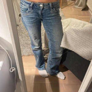 Blå bootcut jeans med slitningar - Säljer ett par blå jeans med bootcut-modell och snygga slitningar. Jeansen har klassisk femficksdesign, låg midja och är tillverkade i denim. Perfekta för dig som gillar en avslappnad och trendig look. Andvänd ganska mycket men väldigt bra skick. Det står ingen lapp men skulle gissa på 164 🤗