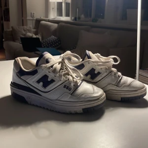 New Balance 550 vita sneakers - Säljer ett par New Balance 550 sneakers i vitt och mörkblått. Klassisk chunky siluett med snörning, perforerade detaljer och tydlig 550-logga på sidan. Ovandel i skinn och mesh för en sportig vibe. Perfekta för dig som gillar retrostil och streetwear. Nypris runt 1200 kr säljer dessa för enbart 250kr