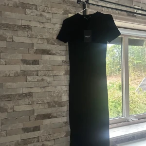 Svart långklänning från ONLY - En stilren svart långklänning från ONLY med rund halsringning och korta ärmar. Klänningen har en rak passform och är tillverkad i ett mjukt material som känns bekvämt mot huden. Perfekt för dig som gillar en enkel och klassisk look.