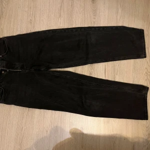 Svarta baggy jeans Jack & Jones - Svarta baggy jeans från Jack & Jones, modell Alex. Jeansen har en lös passform med raka ben och klassiska femficksdetaljer. Tillverkade i denim med snygg tvättad finish och metallknappar. Origellt jeans gjorda för män, men funkar självklart för kvinnor också.