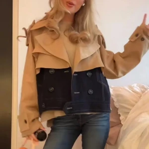 Beige och mörkblå trenchcoat från Zara - INTRESSEKOLL - Unik trenchcoat från Zara i beige och mörkblått med dubbla knapprader och coola detaljer. Jackan har bred krage, axelklaffar och är croppad i modellen. Nedre delen är i mörkblå denim-look med vita sömmar och fickor framtill.