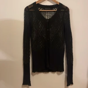 Svart kofta från Tiger of Sweden - Säljer en svart, transparent och stickad kofta från Tiger of Sweden. Koftan har ett snyggt mönster, knappar framtill och är långärmad. Materialet är en mix av mohair, nylon och akryl vilket gör den både lätt och fluffig. Perfekt för lager-på-lager-stil.