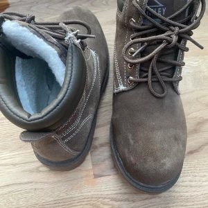 Olivgröna mockaboots från McKinley - Säljer ett par olivgröna boots från McKinley  i mocka med vit kontrastsöm och grov sula. Skorna har snörning och är fodrade med mjukt vitt foder för extra värme. Perfekta för kalla dagar och har en klassisk, robust look.