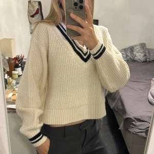 Vit stickad v-ringad tröja H&M - Säljer en vit stickad tröja från H&M med v-ringning och svarta ränder vid halsringning och ärmslut. Tröjan är croppad med breda muddar och har en loose passform. Perfekt för lager-på-lager och chill stil.