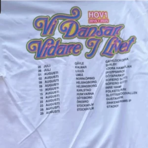 Vit Hov1 turné t-shirt Vi Dansar Vidare - Säljer en vit t-shirt från Hov1 med färgglad text 'Vi Dansar Vidare I Livet' och turnédatum tryckta på framsidan. T-shirten har korta ärmar och är gjord i mjuk bomull, perfekt för dig som gillar svensk musik och vill ha ett minne från turnén. Storlek M men passar S