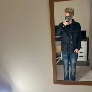 Barbour Jacka  - Säljer en svart quiltad jacka från Barbour i storlek S. Jackan har klassisk design med tryckknappar, dragkedja och flera fickor framtill. Materialet är polyester och jackan har ett snyggt innerfoder med tryck. Perfekt för dig som gillar stilren och tidlös look.