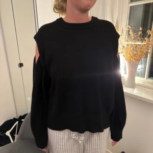 Svart stickad tröja med cut out-detaljer - Svart stickad tröja med coola cut out-detaljer på axlarna. Tröjan har en loose passform och rund halsringning. Perfekt för dig som vill ha en basic men ändå edgy look.