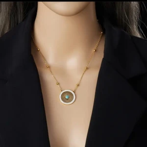 Underbar set med halsband och örhängen med turkos i rostfritt stål med guldtonad  - Snyggt set med halsband och matchande örhängen i guldtonad. Båda har rund form med ett detaljerat, genombrutet mönster och en turkos sten i mitten. Halsbandet har en cirkel dekorerad med små glittriga stenar runt kanten. Perfekt för dig som gillar unika smycken med färg.